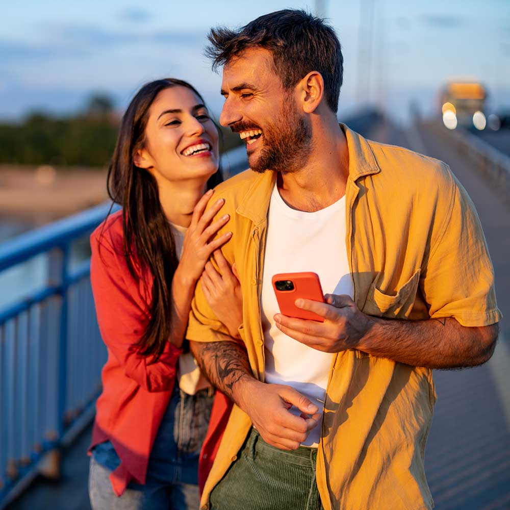 A happy couple smile while walking over a bridge at sunset